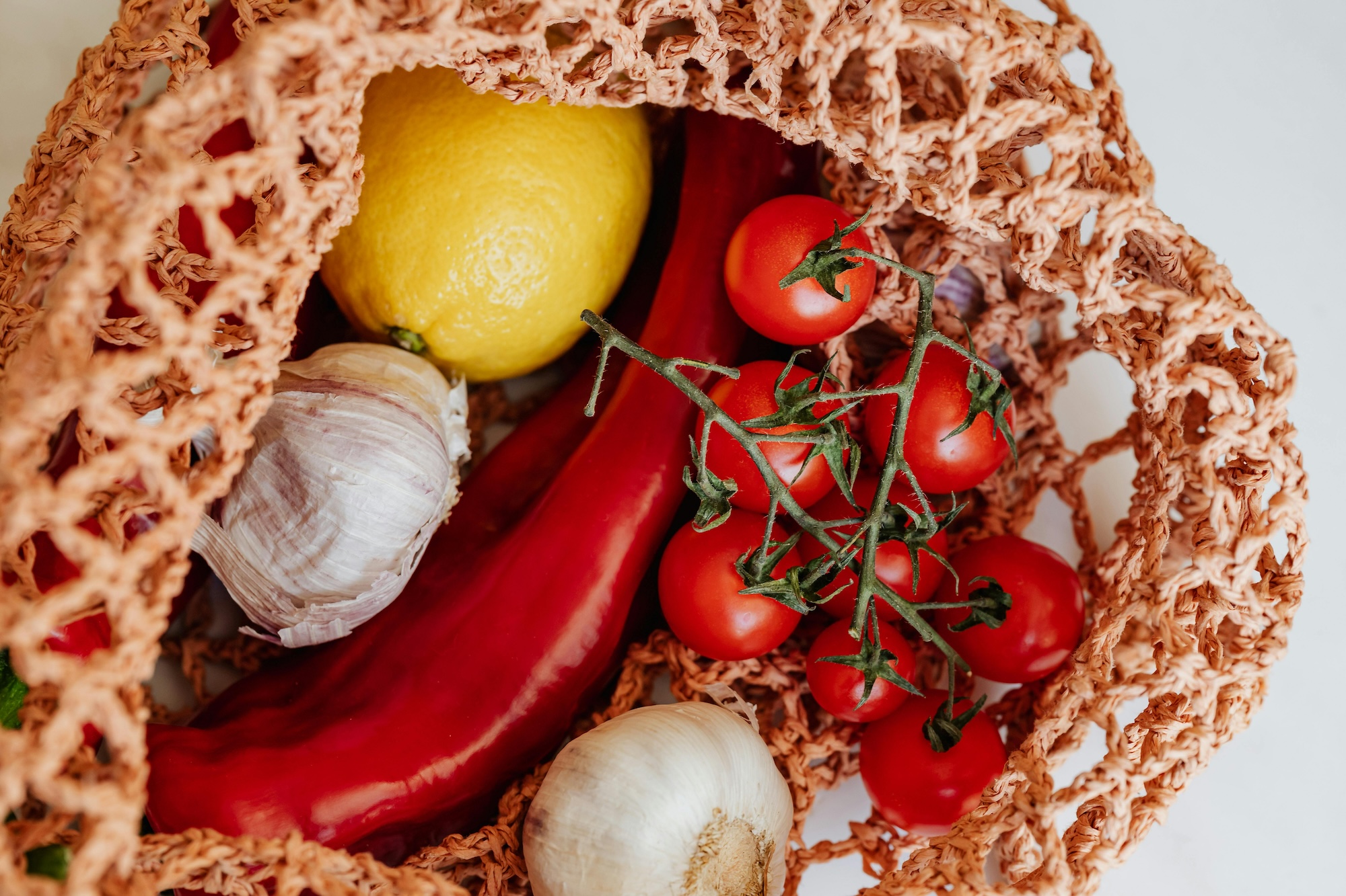 A mesh grocery bag with a lemon, garlic, tomatoes and peppers